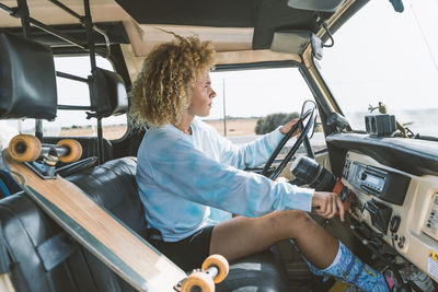 Young blond afro woman sitting by skateboard while driving old off-road vehicle