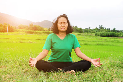 Woman meditating in lotus position on field against sky