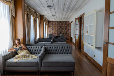 Young woman sitting on sofa reading a book