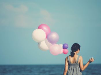 Rear view of woman with balloons in sea against clear sky