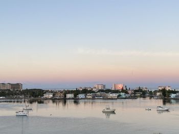 Boats in sea against buildings in city at sunset