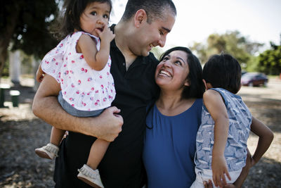 Happy couple carrying children while standing at park