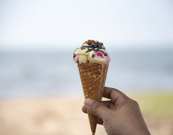 Midsection of person holding ice cream against sea