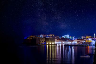 Illuminated buildings by sea against sky at night