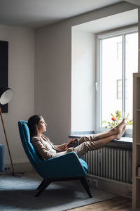 Thoughtful businesswoman sitting on chair with feet up at home