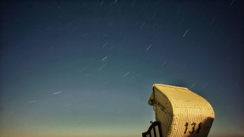 Scenic view of star trails over hooded beach chair against sky at night