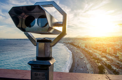 Coin-operated binoculars by sea against sky in city
