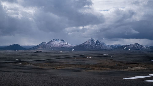 Scenic view of landscape and snowcapped mountains against cloudy sky