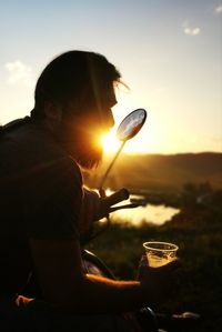 Young man holding disposable glass on motorcycle at sunset