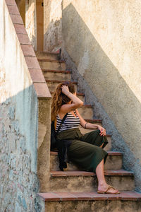 Woman sitting on staircase against wall