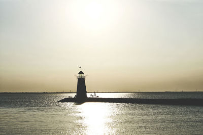 Lighthouse by sea against clear sky during sunset