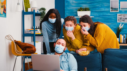 Cheerful people wearing mask looking at laptop at home