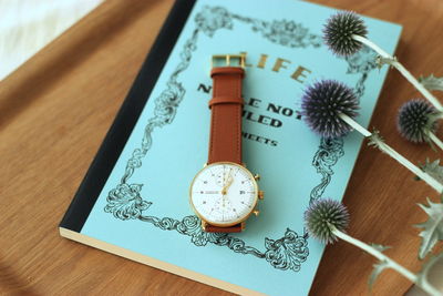 High angle view of wristwatch and book with onion flowers on table