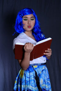 Portrait of a woman reading book against gray background