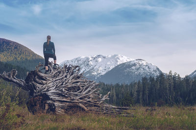Rear view of woman standing on log at forest against cloudy sky