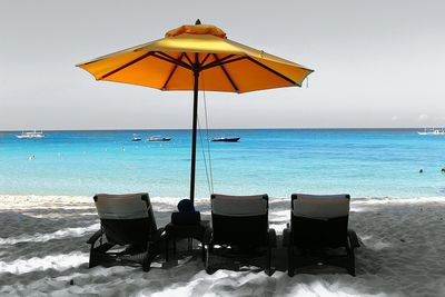 Empty deck chairs by parasol at beach against sky