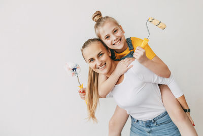 Beautiful and happy mom and daughter paint the walls in the apartment white