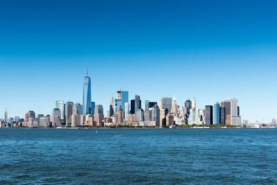 Sea by modern buildings against clear blue sky