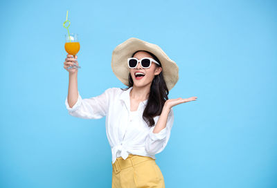 Young woman wearing sunglasses standing against blue sky