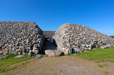 Stone wall on field against clear blue sky