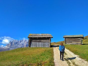 Rear view of woman walking on dirt road against clear blue sky