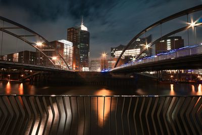 Illuminated bridge over river against buildings at night