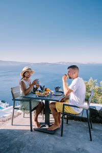 Young couple sitting on chair by sea against sky