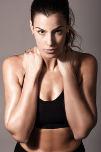 Portrait of confident female athlete standing against gray background