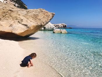 Child playing by rock by sea against clear sky