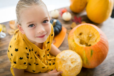 Portrait of cute girl sitting by pumpkin at home