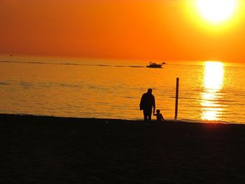 Silhouette people standing on beach against orange sky