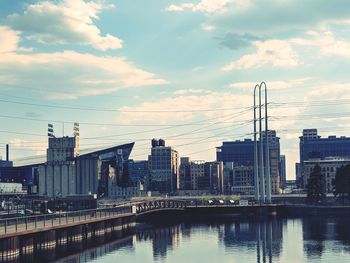 Bridge over river by buildings in city against sky