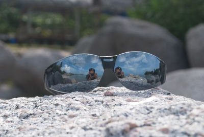 Man photographing with camera reflecting on sunglasses at rock at beach