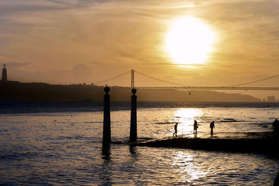 Silhouette bridge over sea against sky during sunset