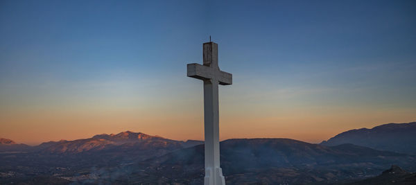 Cross against mountains during sunset