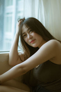 Young woman looking away while sitting on window at home