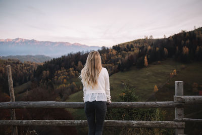 Rear view of woman standing on railing against sky