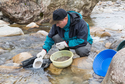 Man sitting on rock by stream