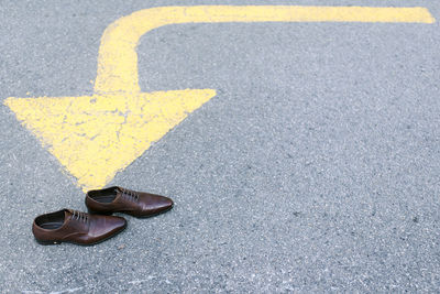 High angle view of arrow sign and shoes on road
