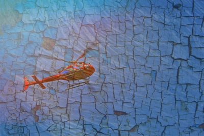 Low angle view of red helicopter flying against patterned wall on sunny day