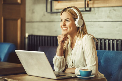 Portrait of smiling young woman using phone while sitting on table