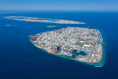 High angle view of sea by cityscape against blue sky
