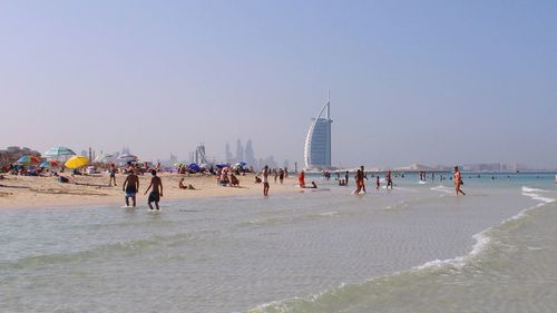 People enjoying at jumeirah beach against burj al arab hotel