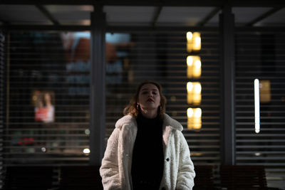Portrait of young woman standing in city during winter at night