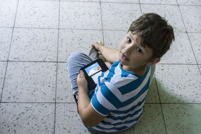 Portrait of cute boy sitting on tiled floor while holding video game at home
