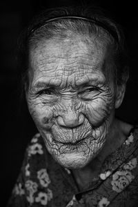 Close-up portrait of wrinkled senior woman against black background