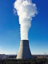 Smoke emitting from factory against blue sky