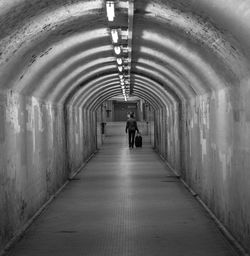 Rear view of man walking with suitcase in illuminated tunnel