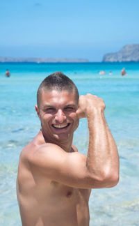 Portrait of smiling shirtless man flexing muscles at beach