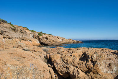 Scenic view of rocky beach against clear blue sky